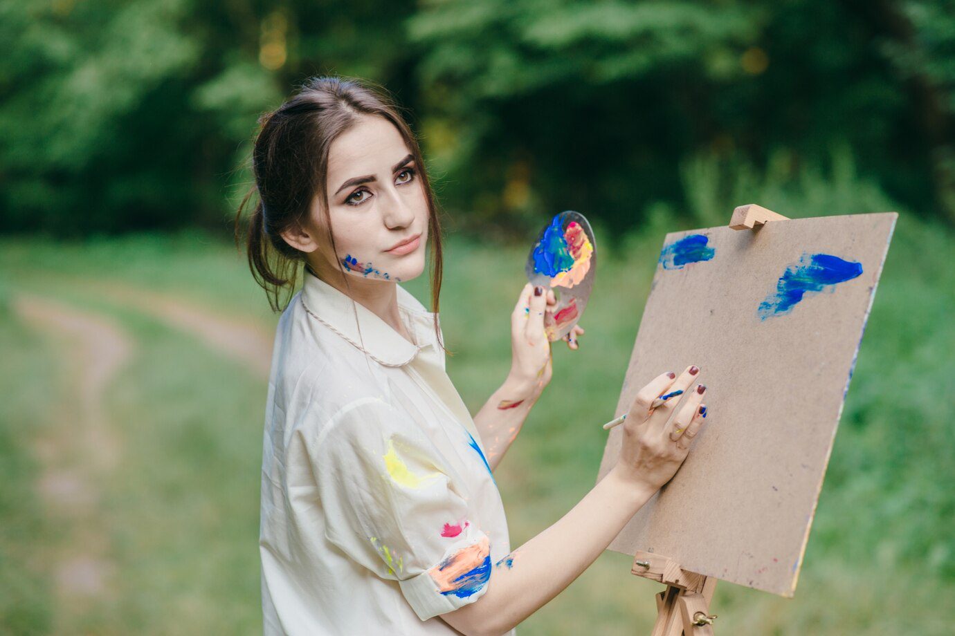 A woman holding a paintbrush and painting on a canvas.