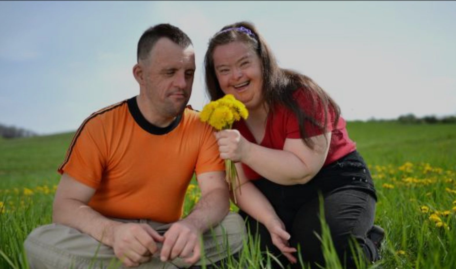 A man and woman sitting in the grass holding a flower.